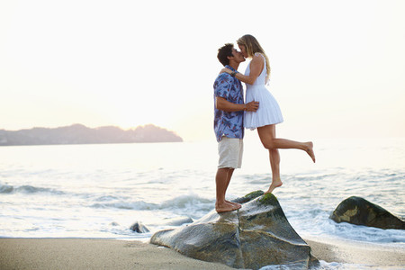 Affectionate romantic young couple kissing on ocean rock 01