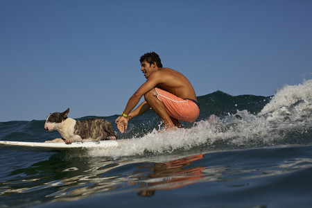 Young man and dog riding surfboard on ocean wave 01