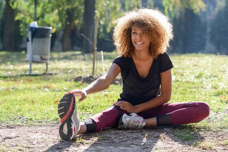 Fitness black woman runner stretching legs after run