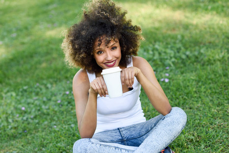 Woman with afro hairstyle drinking coffee in park