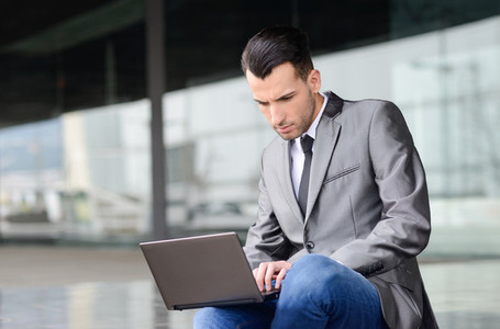Young businessman typing in a laptop computer in urban backgroun