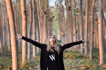 Happy woman playing with autumn leaves in forest