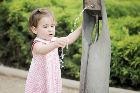 Little girl drinking water in a park fountain