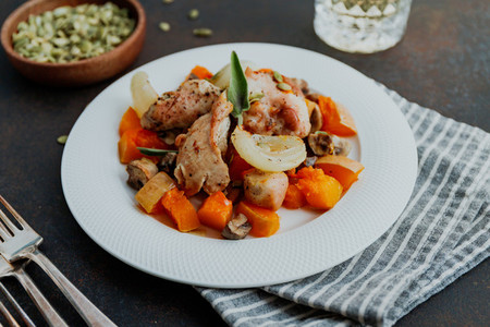 Seasonal autumn low calorie recipe from baked turkey medallions with pumpkin  onion  champignons and sage on a white plate