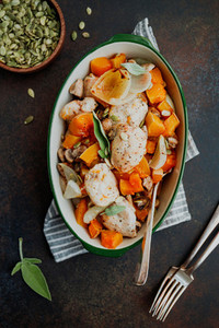 Top view on seasonal autumn low calorie recipe from baked turkey medallions with pumpkin  onion  champignons and sage in a ceramic dish