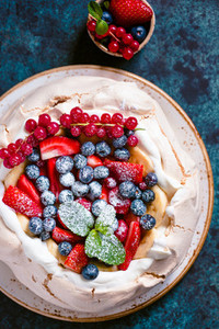 New Zealand Pavlova cake with whipped cream and mix of fresh berries on a blue textured background