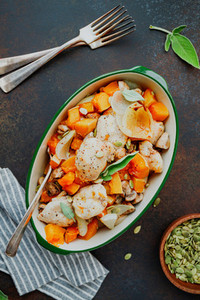 Top view on seasonal autumn low calorie recipe from baked turkey medallions with pumpkin  onion  champignons and sage in a ceramic dish