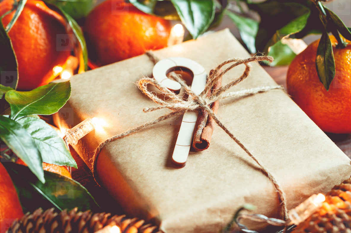 Christmas gift box in a kraft paper among tangerines and fir cones on a festive table  The concept of cosy winter Holidays