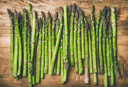 Raw uncooked green asparagus in row over wooden background