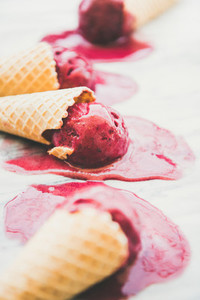 Raspberry sorbet ice cream scoops in waffle cones  selective focus