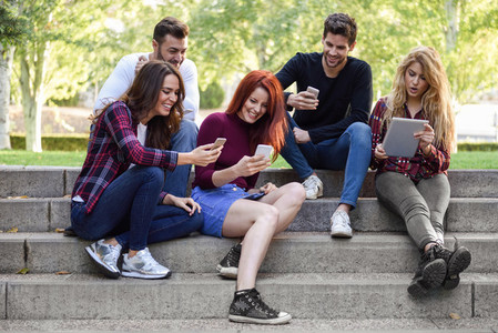 Young people using smartphone and tablet computers outdoors