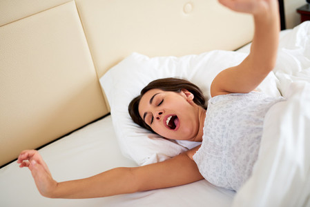 Woman yawning and stretching arms in bed