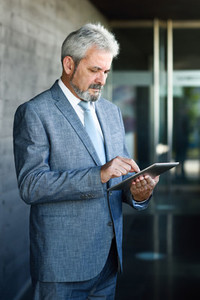 Senior businessman with tablet computer outside of modern office