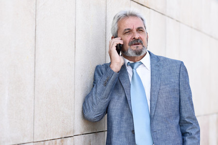 Senior businessman with smartphone outside of modern office buil