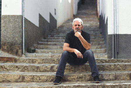 Mature man with white hair sitting on urban steps