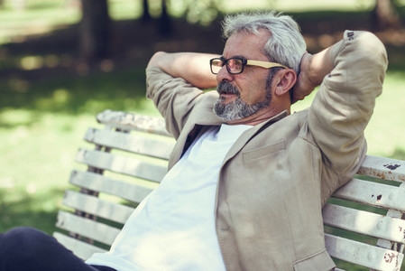 Pensive mature man sitting on bench in an urban park