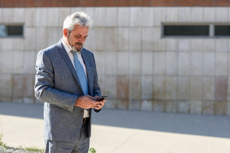 Senior businessman texting with smartphone outside of modern off