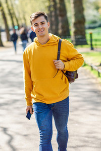 Young urban man using smartphone walking in street in an urban park in London
