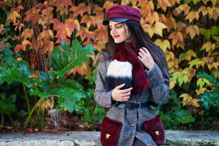 Young girl with very long hair smiling and wearing winter coat and cap in autumn leaves background