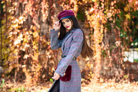 Young beautiful girl wearing winter coat and cap in autumn leaves background