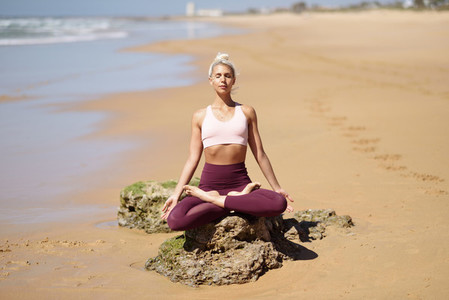 Caucasian blonde woman practicing yoga in the beach