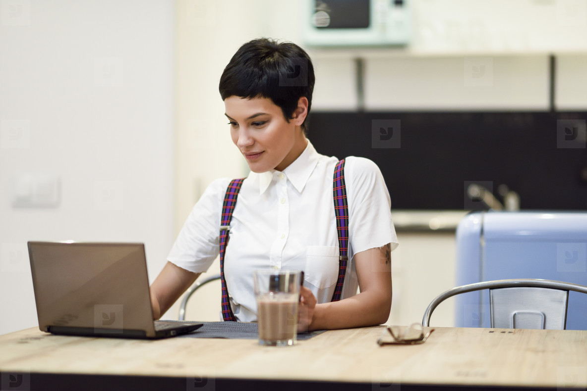 Young woman with very short haircut typing with a laptop at home