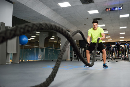 Man with battle ropes exercise in the fitness gym