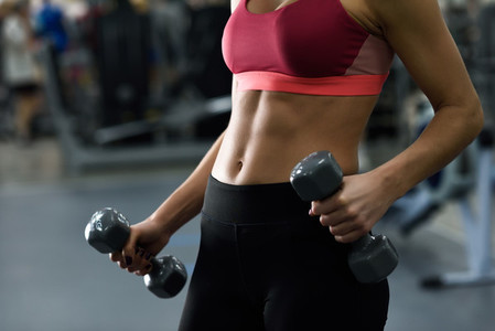 Young woman with beautiful abdomen lifting dumbells at gym