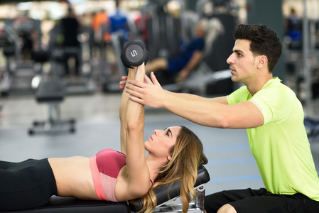 Personal trainer helping a young woman lift weights