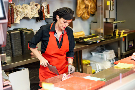 Female butcher cutting meat at counter in butchery