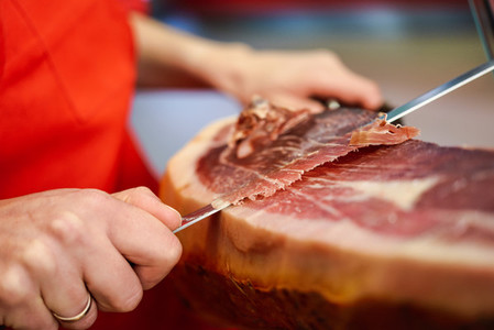Professional cutter carving slices from a whole bone in serrano ham
