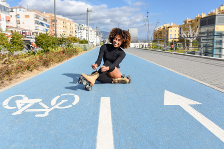 Young smiling black girl sitting on bike line and puts on skates