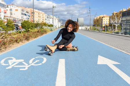 Young smiling black girl sitting on bike line and puts on skates
