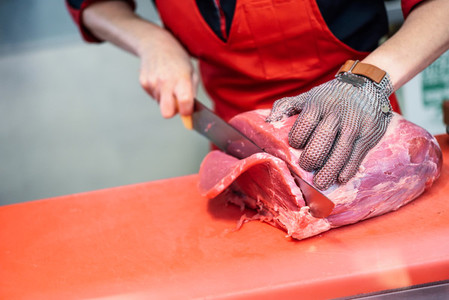 Woman cutting fresh meat in a butcher shop with metal safety mes