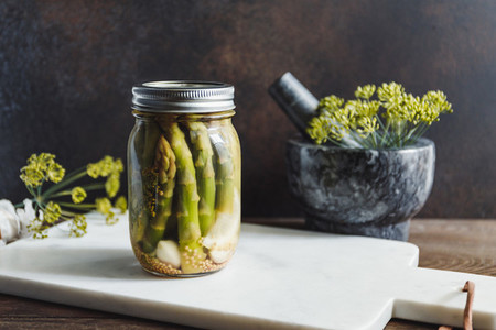 Pickled asparagus in a glass jar on a white marble tray  Seasonal canning vegetable recipe