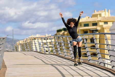 Afro hairstyle woman on roller skates riding outdoors on urban bridge