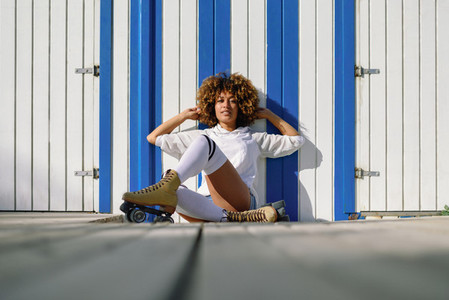 Young black woman on roller skates sitting near a beach hut