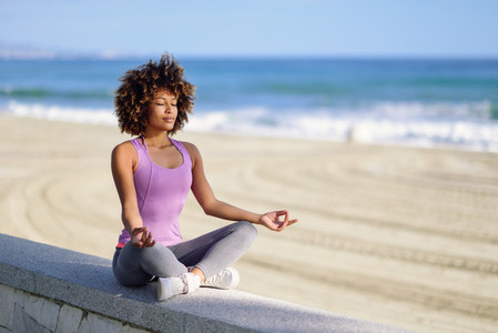 Black woman afro hairstyle in lotus pose with eyes closed in the beach