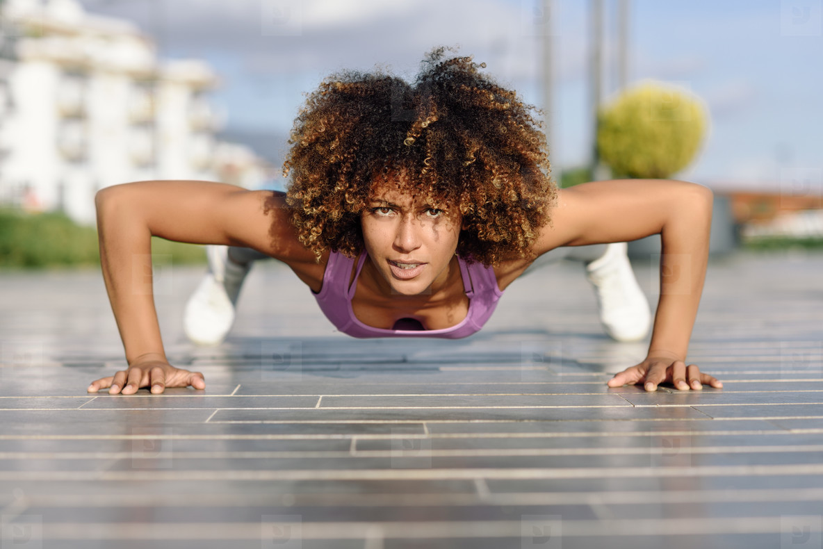 Black fit woman doing pushups on urban floor