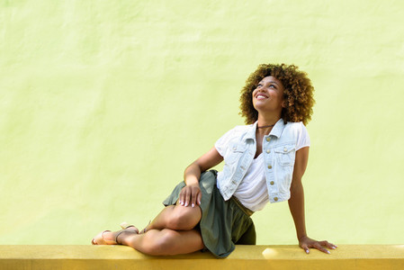 Young black woman afro hairstyle sitting on an urban wall
