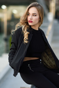 Beautiful young girl wearing black jacket sitting in the street