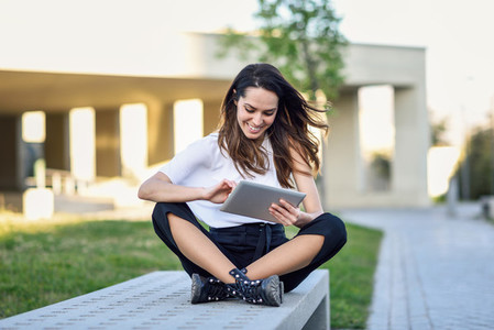 Young woman using digital tablet sitting outdoors in urban background