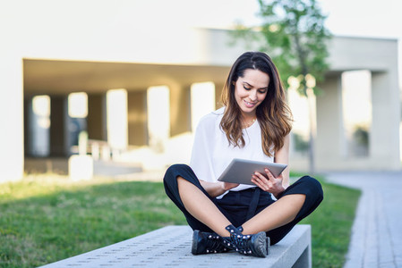 Young woman using digital tablet sitting outdoors in urban background