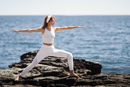 Young woman doing yoga in the beach wearing white clothes
