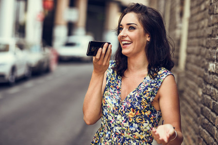 Smiling young woman recording voice note in her smart phone