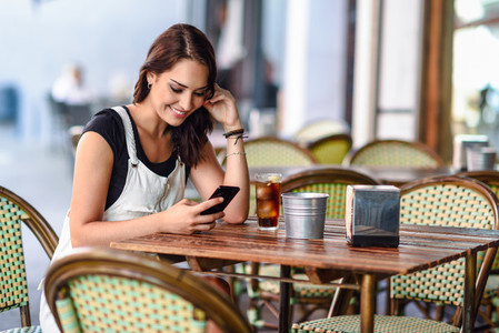 Girl with blue eyes sitting on urban cafe using smart phone smil
