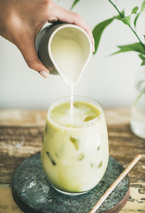 Iced matcha latte drink with milk pouring from pitcher  close up