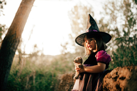 Girl standing disguised as a witch in the woods during Halloween