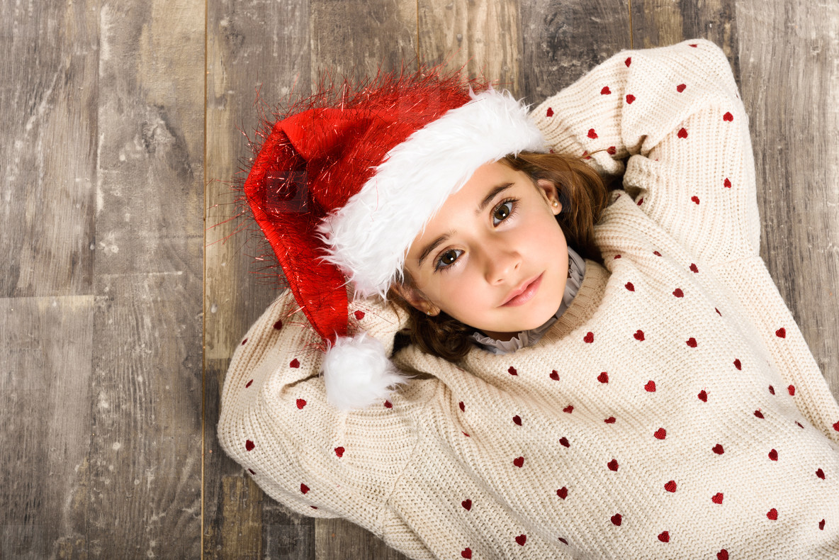 Adorable little girl wearing santa hat laying on wooden floor