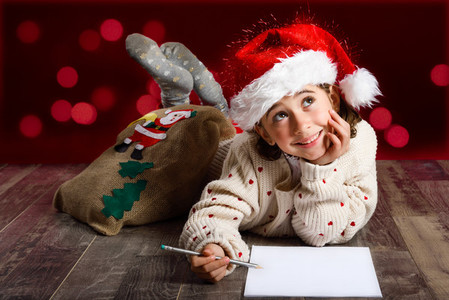 Adorable little girl wearing santa hat writing Santa letter